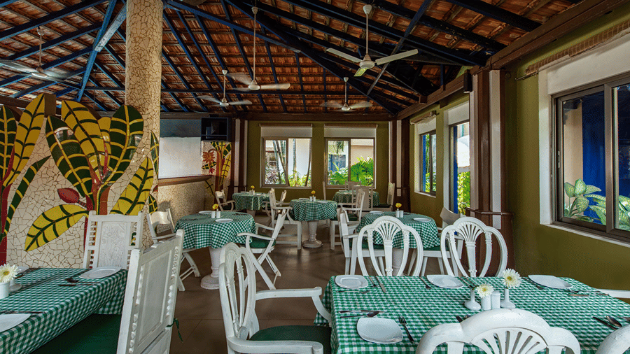 Open-air dining space with green checked tablecloths, white chairs and large windows overlooking greenery.