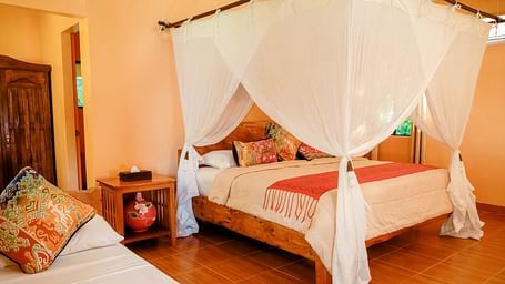 Room at Flower Island Resort with a canopy bed, pillows, wooden nightstand, and soft lighting.