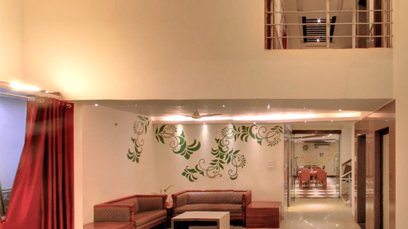 A spacious hotel suite lounge featuring a brown sectional sofa and an open loft area above.