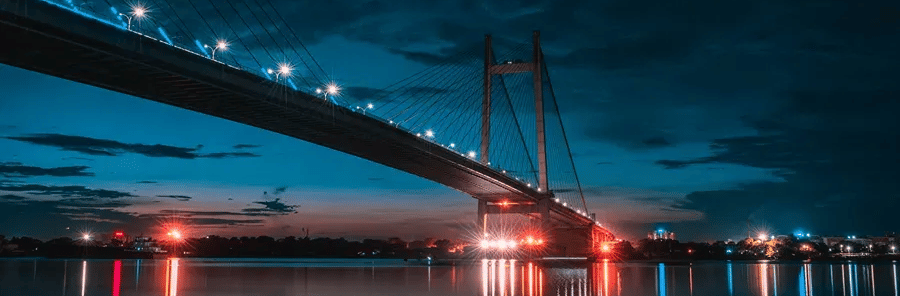 howrah bridge over a waterbody with light in the background.