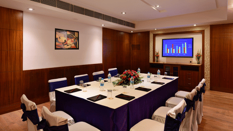 Board room with royal blue seating arrangement, bright lighting, flat screen TV, and wooden flooring.
