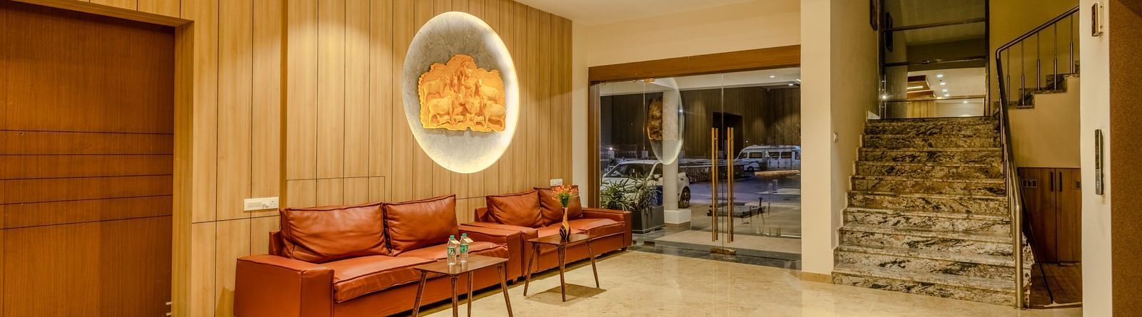 A wide angle shot of an inviting lobby area at Daksh The Grand Gowardhan, Dwarka, with plush seating, elegant decor, and a view of the outside.