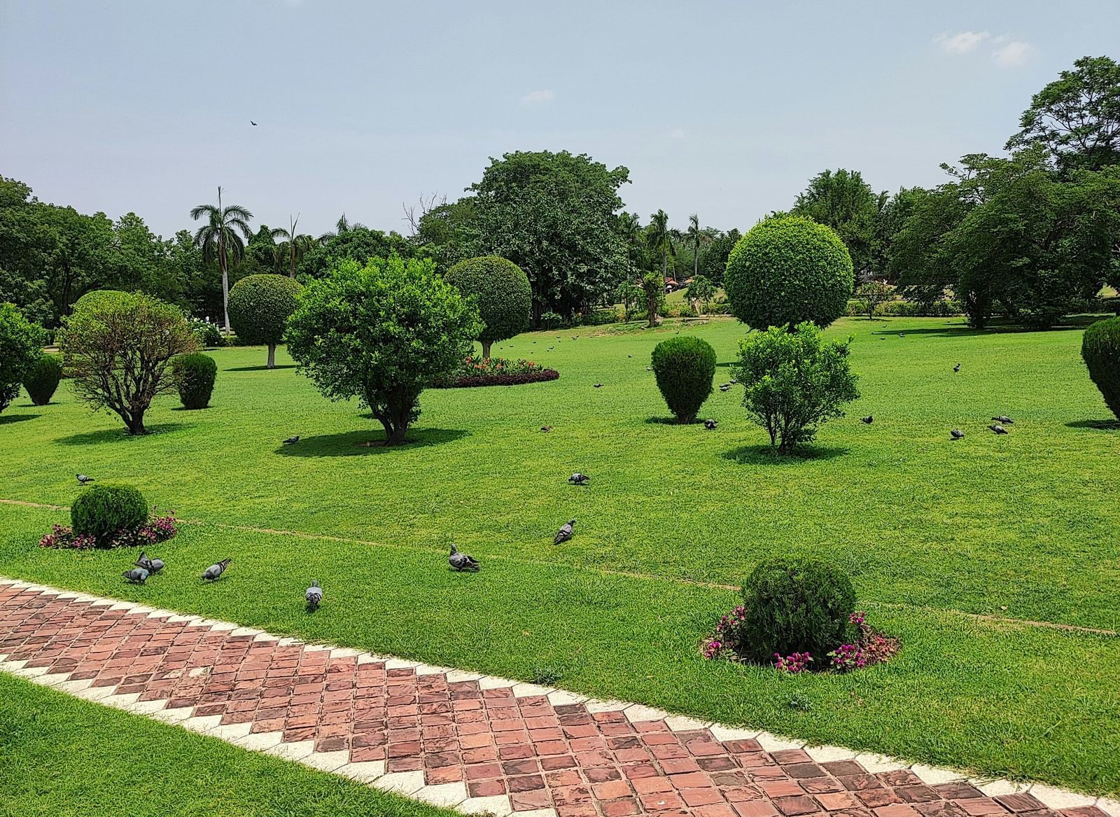 Manicured green park or garden with a red brick pathway lined by stepped grass banks.