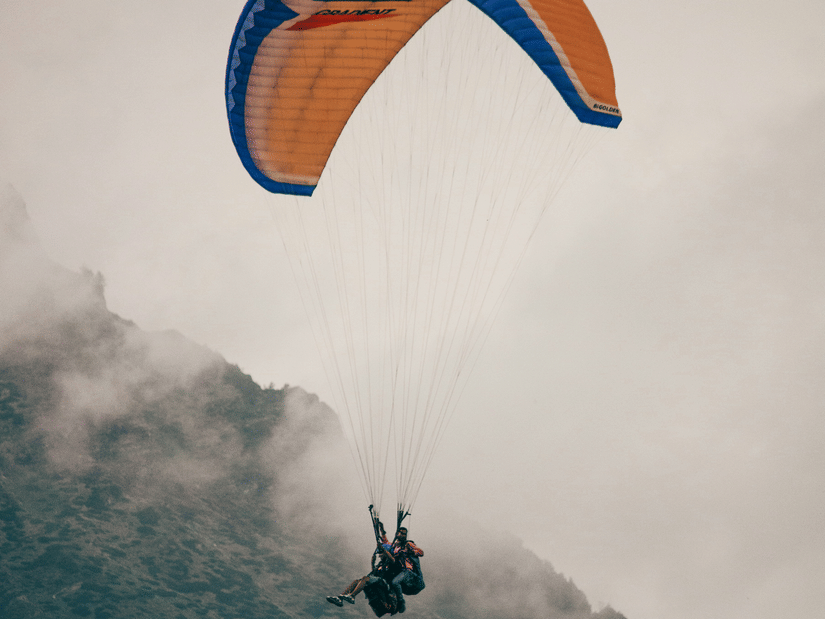 A person paragliding by holding the strings on the parachute and fog over a mountain in the background.
