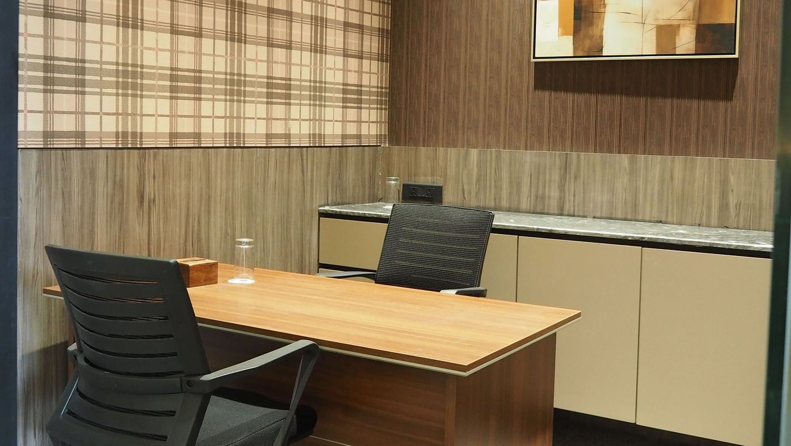 A small desk with a computer and a lamp, against a checkered wall with artwork - Club Charholi, Pune 