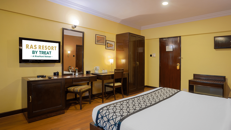 A well-furnished executive room at Ras Resort by Treat, Silvassa, featuring a comfortable bed, a dressing table, and a television.