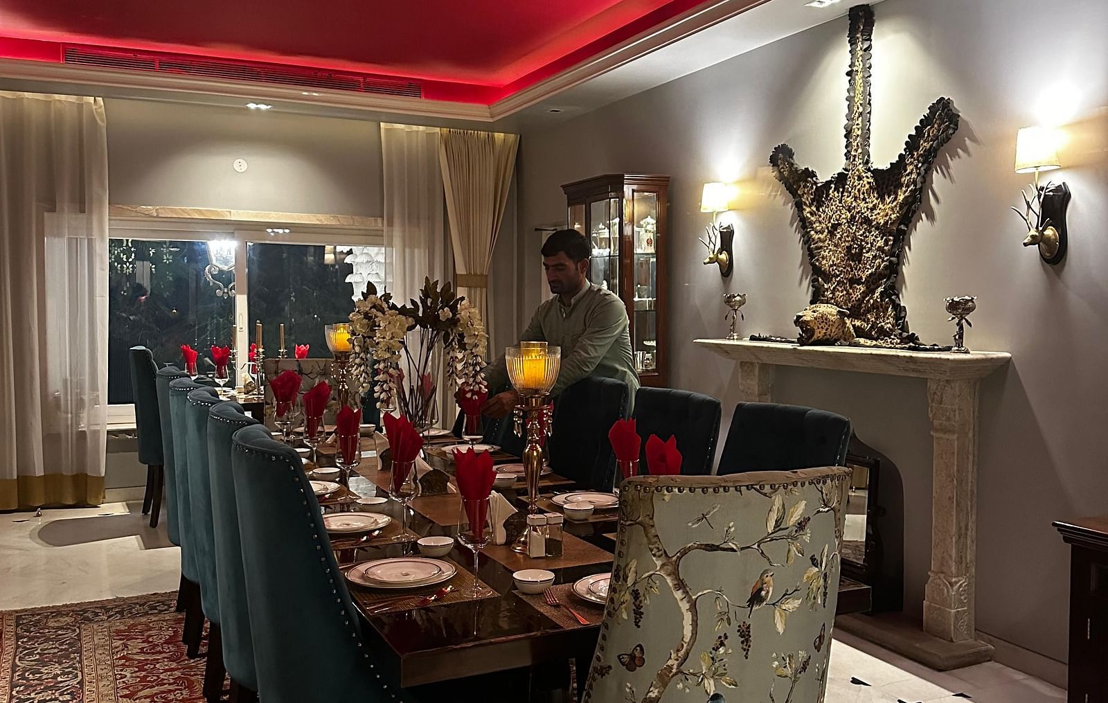 A long dining table set with plates and cutlery, under a red ceiling with neon lighting, in a room with grey walls and decorative wall sconces | Dileep  Kothi, Jaipur