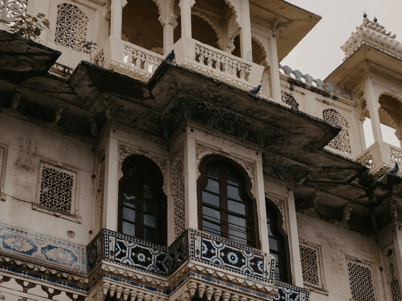 Ornate carved balcony on Udaipur City Palace, with domed turrets above.