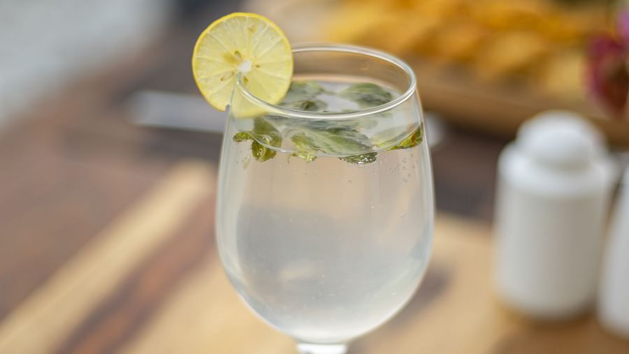 Refreshing drink with mint and lemon in a wine glass, served alongside colorful appetizers and garnishes at The Bridge, Clarks Inn Suites Jaipur