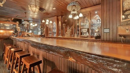 A warmly lit wooden bar at Shaver Lake Village Hotel with classic decor, vintage hanging lamps, and barstools lined along the counter.
