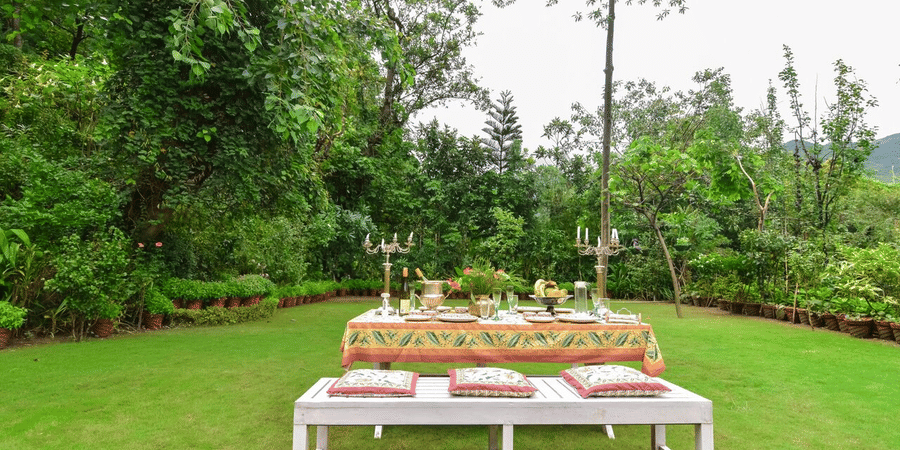 A view of a lawn area with a seating arrangement for dining placed on it and trees surrounding the area at Shaheen Bagh.
