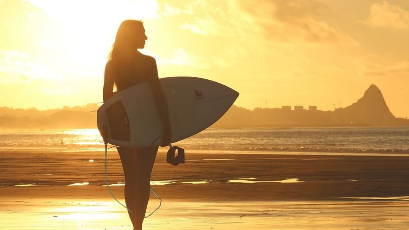 a woman carrying a surf board by the beach
