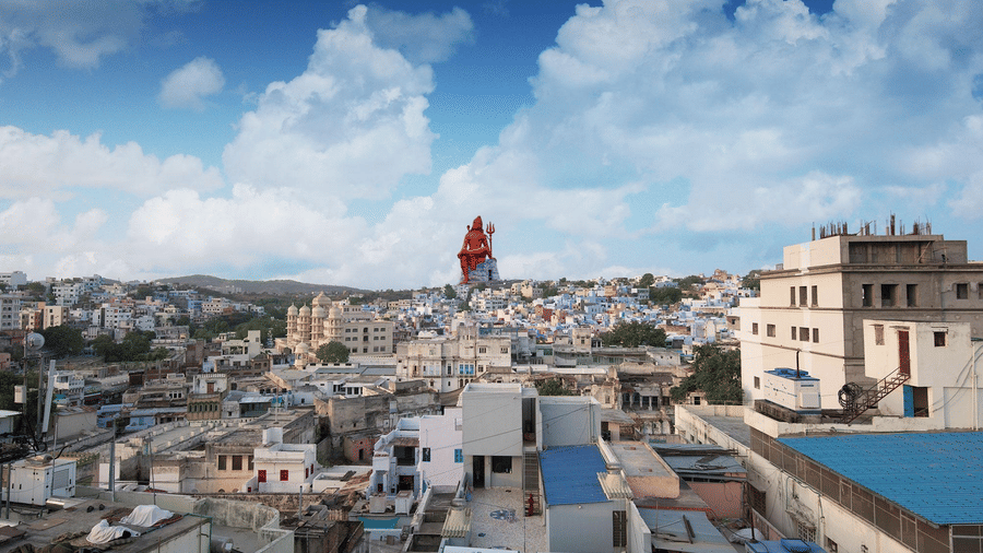 City skyline view from Sanmukh by Adamo, with a towering seated Shiva statue rising above the rooftops under a cloudy sky.