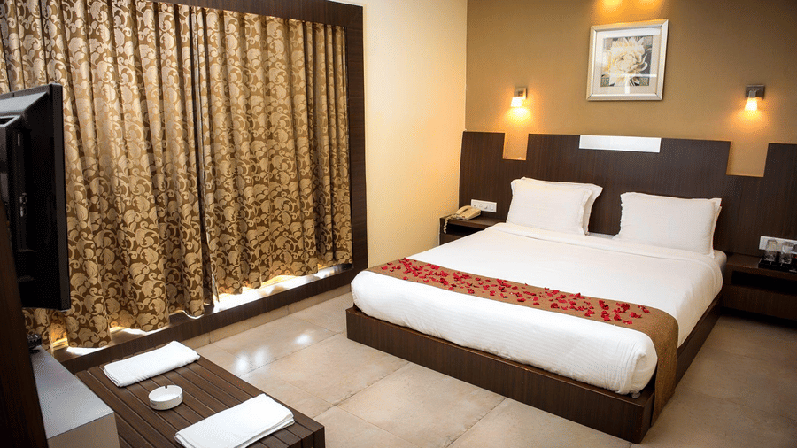 The Regent Deluxe room of the hotel with a neatly made bed with a red runner on it, two side tables, a wall mounted TV, and a console in front.