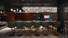 A sleek bar lounge featuring green bar stools and ambient lighting, designed for upscale dining and drinks.