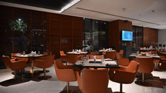 A contemporary dining area with round tables and orange chairs set against a warm, wooden backdrop.