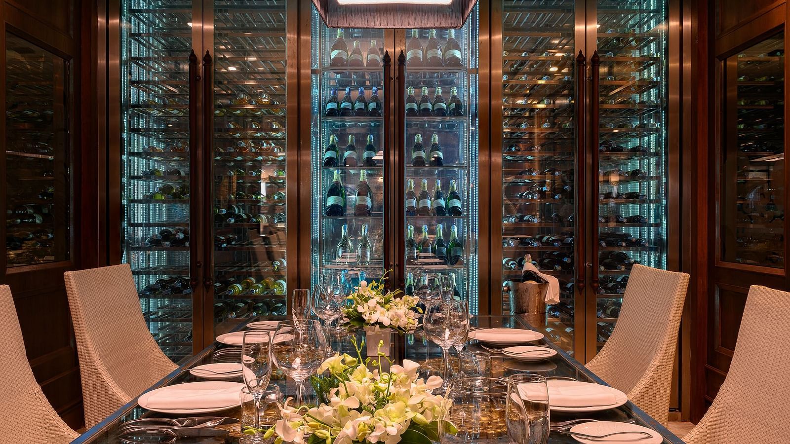 A beautifully set dining table along with the wine cellar in the background - Maikhao Dream Villa Resort & Spa, Phuket 