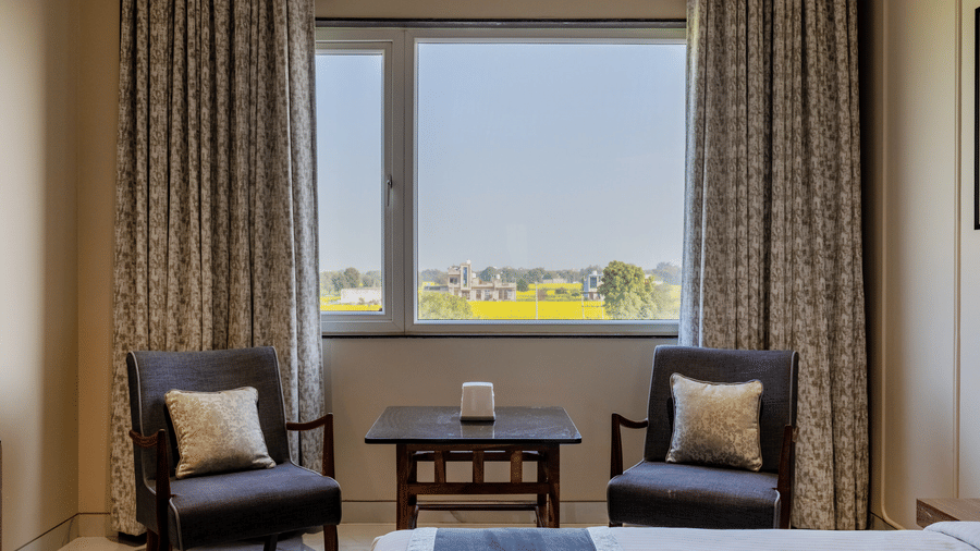 A room at Hotel Highway Prince, Behror, featuring two armchairs and a small table by a large window with floor-to-ceiling curtains.