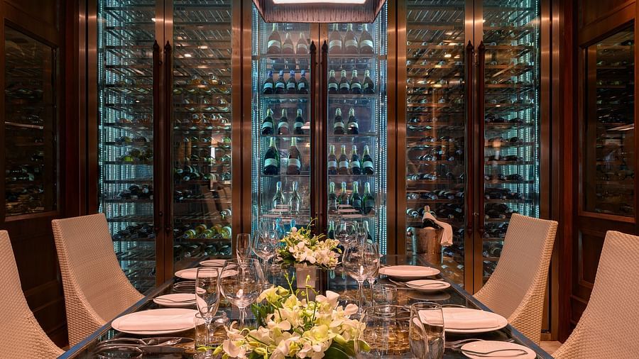 A beautifully set dining table along with the wine cellar in the background - Maikhao Dream Villa Resort & Spa, Phuket 