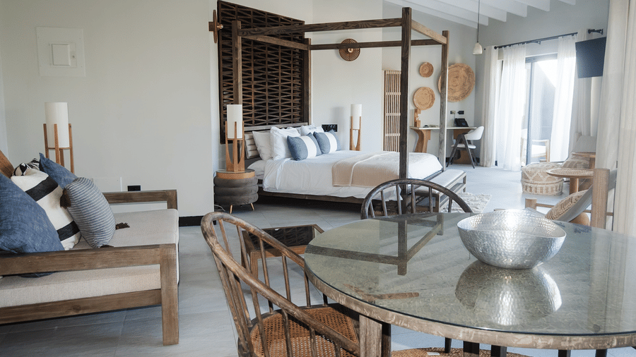 A bedroom with a king bed, a table with a bowl, chairs, a sofa, and sliding glass doors at Tamarind Hills Resort and Villas, Antigua.