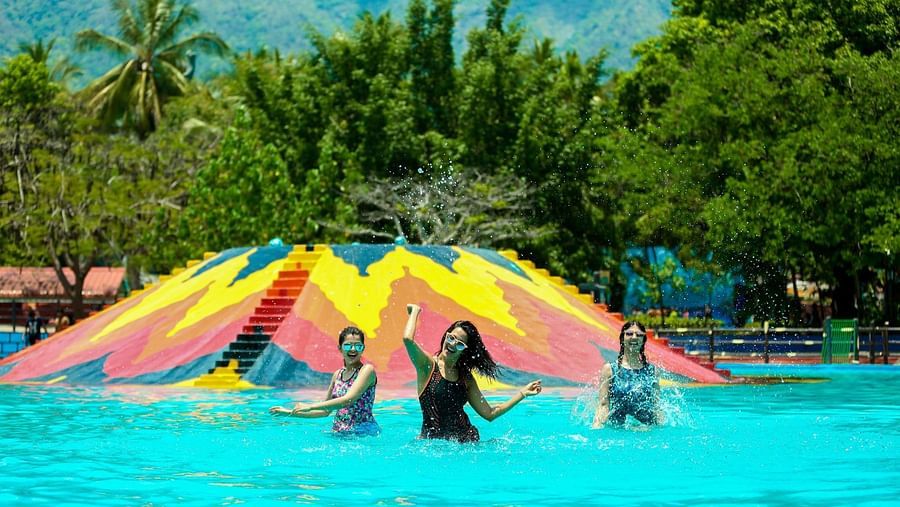People splashing and enjoying in a swimming pool at Black Thunder surrounded by lush green trees in the background