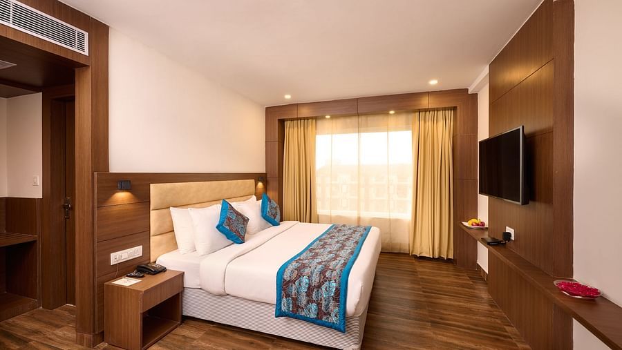 A contemporary hotel room at Renest Haridwar features a bed with decorative pillows and a patterned runner, bedside tables with lamps, a mounted television, and wooden flooring - Renest Haridwar
