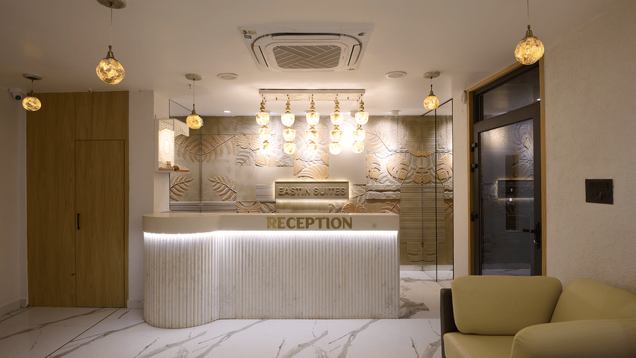 A hotel reception area with a curved white counter, pendant lighting hanging above the counter, and modern marble flooring | Voyage Eastin Suites