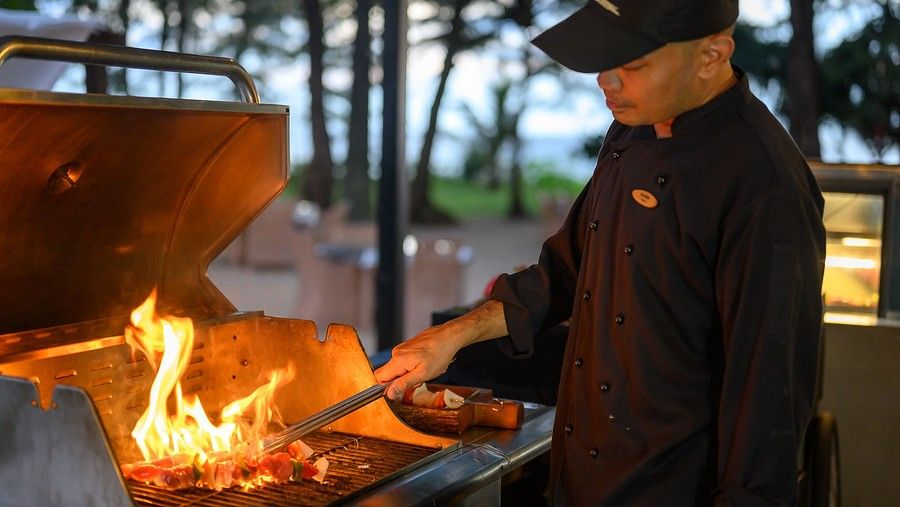 image of a person roasting skewers on a barbecue at maikhao dream villa resort and spa, phuket