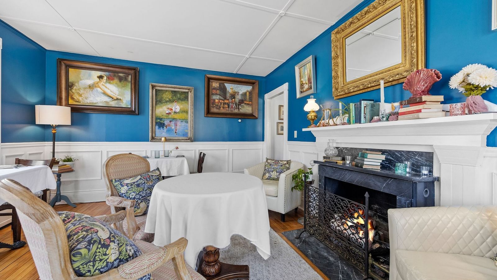 Dinning room at Hartstone Inn with teal walls, fireplace, white table settings, and elegant framed artwork.