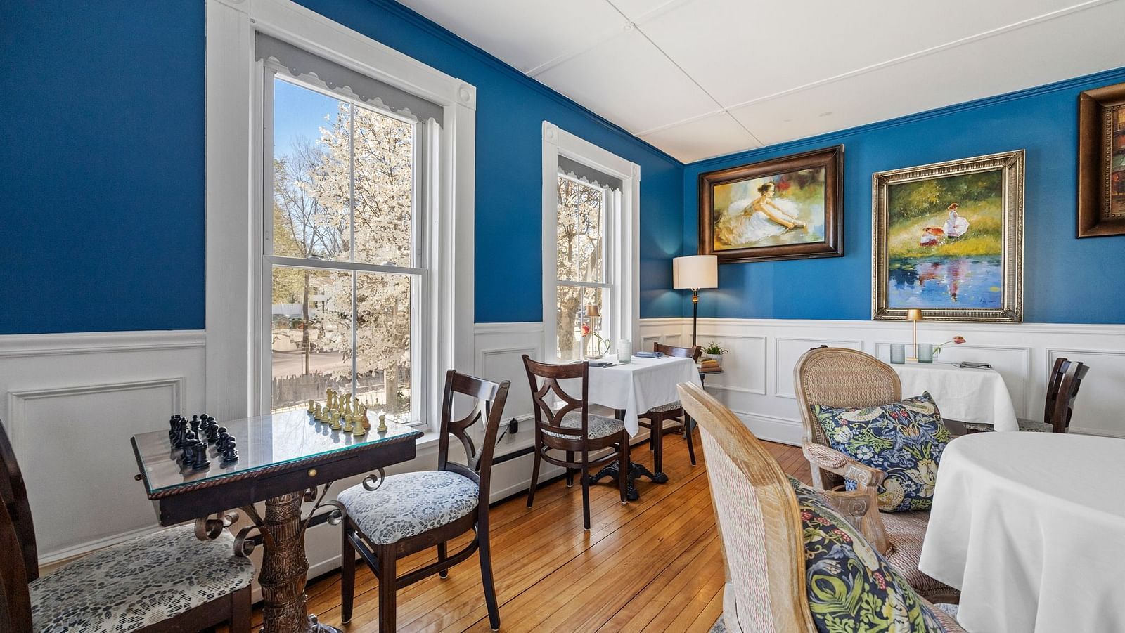 Dinning room  at Hartstone Inn with blue walls, white wainscoting, and large windows, furnished with antique-style chairs and tables.