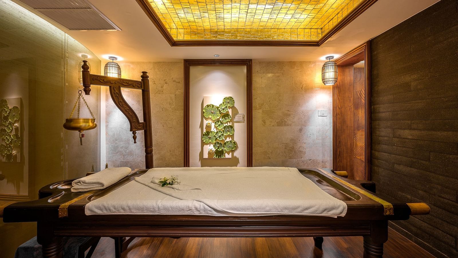 A wooden massage bed in the middle of the room accommodated in an ambient setting at Maikhao Dream Villa Resort & Spa, Phuket