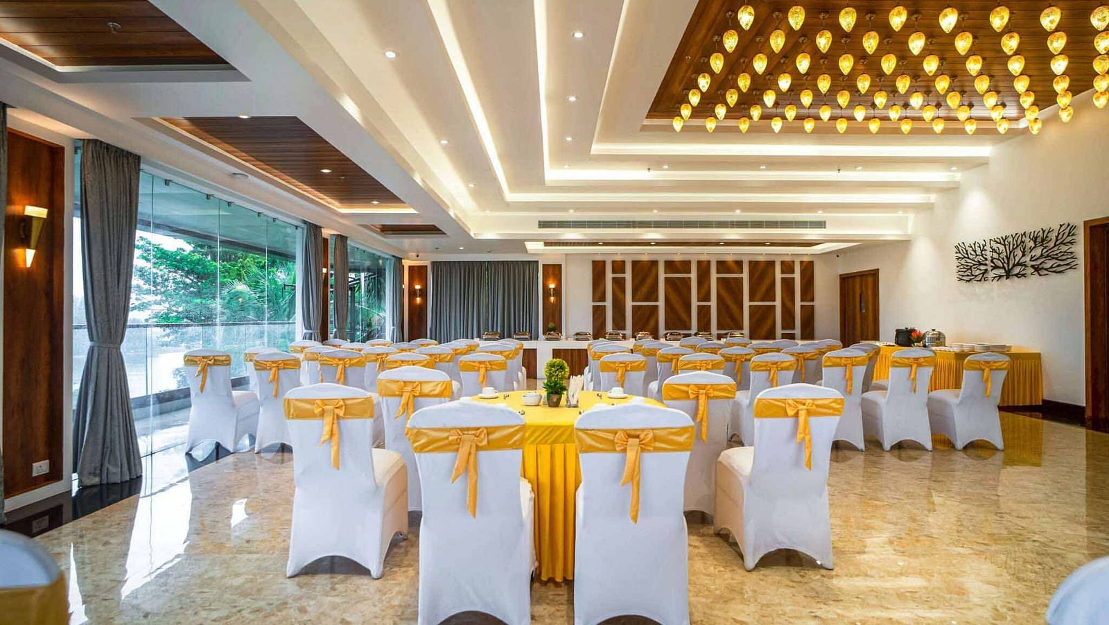 A spacious and brightly lit event hall at Mansha Palace is arranged with round tables and draped chairs.