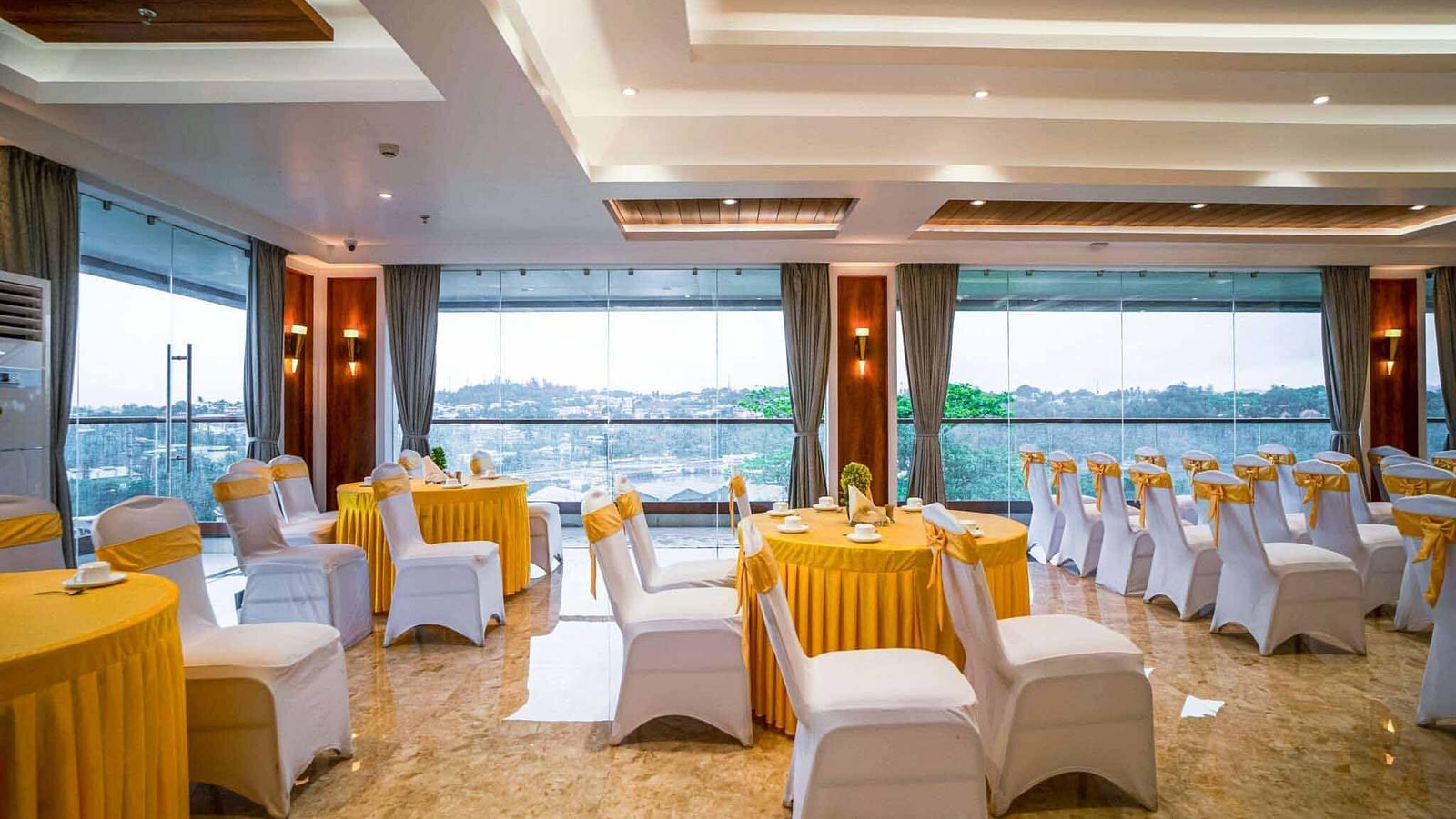 A bright event space at Mansha Palace offers city views through large windows and is furnished with set tables and chairs.