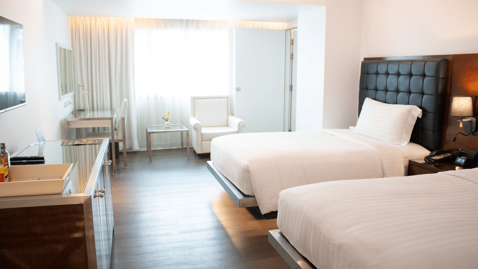 Spacious room with twin beds, wooden floor and curtained window at Night Hotel Bangkok, one of the perfect Guest Friendly Hotels in Bangkok Near Nana Plaza.