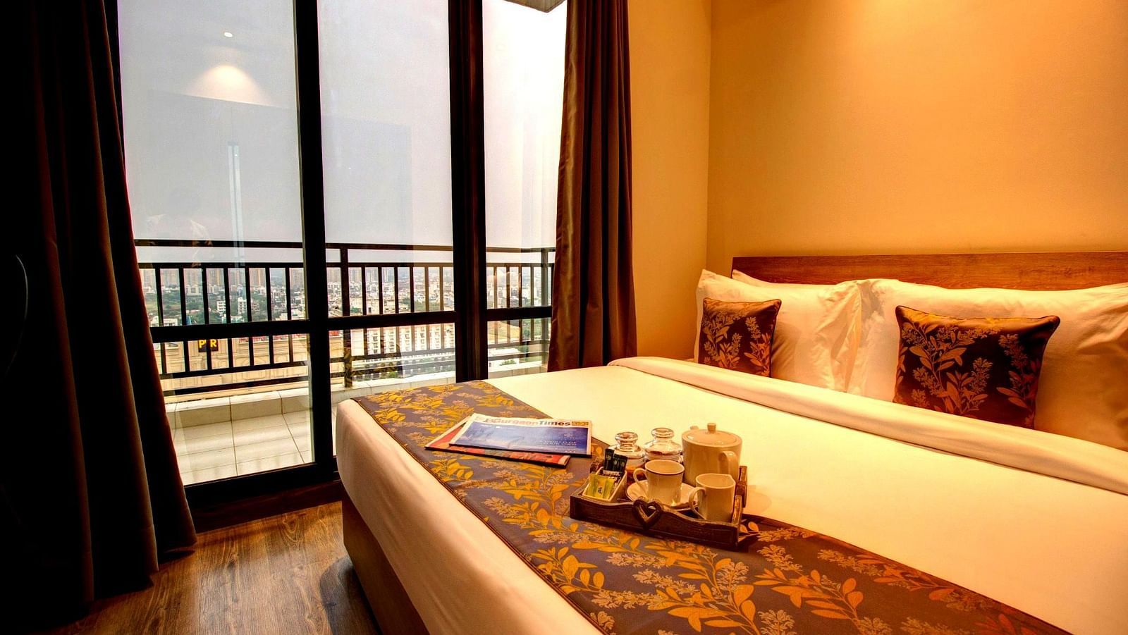 An overview of the premium suite with a double bed next to large glass windows - Rhythm Gurugram.