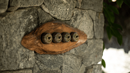 A unique, organically shaped wooden electrical switch plate mounted on a rugged stone wall at Earthitects