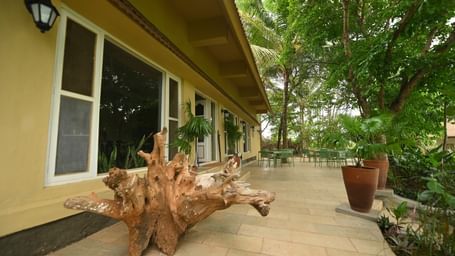 Fireflies Resorts exterior with a tiled walkway, potted plant, and large wooden log decor placed beside glass windows under a yellow roof.