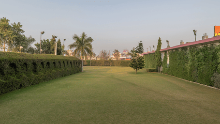 Hotel Highway Prince Paota vast open green lawn with manicured hedges, palm trees, and clear blue sky in a serene daytime setting.