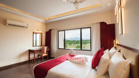 A bright hotel room featuring a large bed with red accents and a window offering a scenic outdoor view - Jenneys Residency, Coimbatore