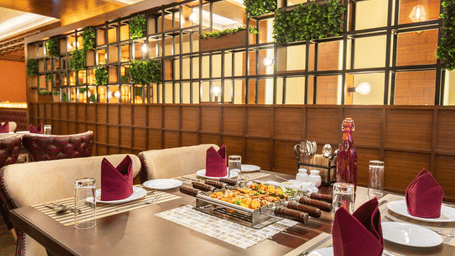 A dining table prepared with a central grill, formal dinnerware, and decorative wall greenery - Jenneys Residency, Coimbatore.