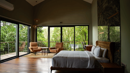 A spacious bedroom with polished wood floors, a large bed, and floor-to-ceiling glass doors leading to a forest balcony at Stanley Revelation.