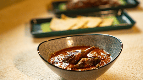 A close-up shot of a rich red chicken curry served in a grey ceramic bowl on a light-coloured counter at Stanley Revelation.