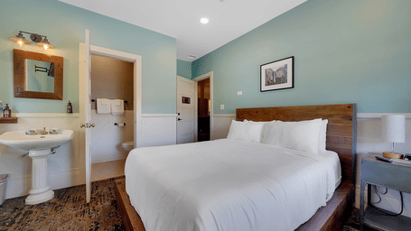 One of our rooms near Yosemite National Park, featuring sage green walls, a wooden bed with crisp white bedding, and a pedestal sink with mirror.
