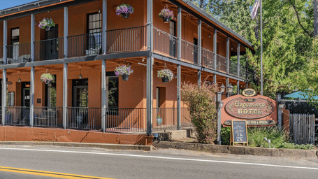 Historic Groveland Hotel exterior on Main Street featuring the 1849 Monterey Colonial style adobe building with a wraparound porch and classic wooden signage in Groveland, California.
