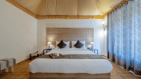 Swiss tent bedroom with draped curtains at Valley by Grassfield, a tented resort in Jaipur.