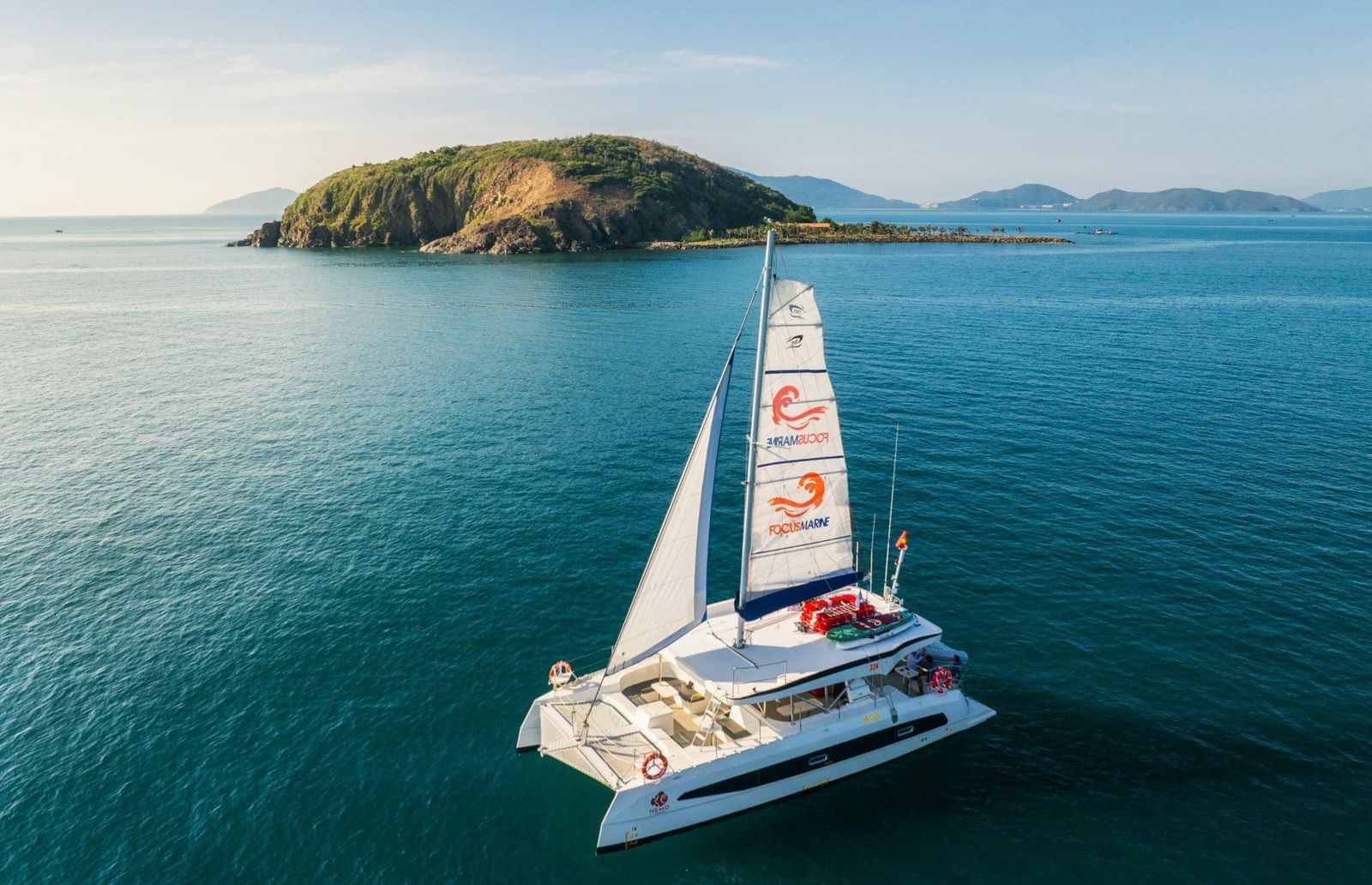 A sleek catamaran sailing on turquoise waters with island views, offering scenic marine adventures from Alibu Resort.