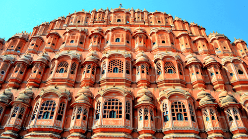 The intricate windows of the Hawa Mahal in Jaipur getting highlighted by the bright sun rays against a clear blue sky in the background.