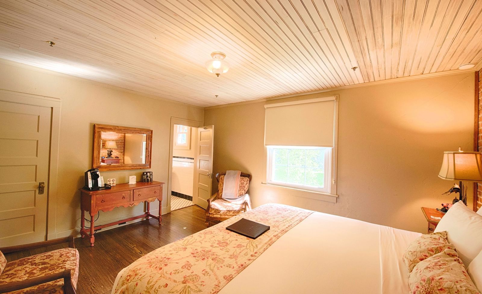 side view image of a bedroom highlighting the smooth sheets spread over the double bed along with a wooden table opposite to it - Historic Tapoco Lodge 