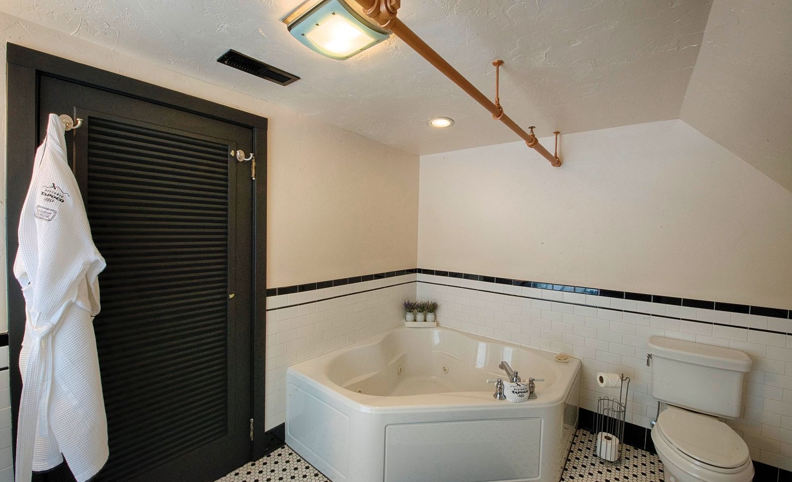 a luxurious bathroom featuring a full size bathtub beside a huge black door with a bathrobe hanging over it - Historic Tapoco Lodge