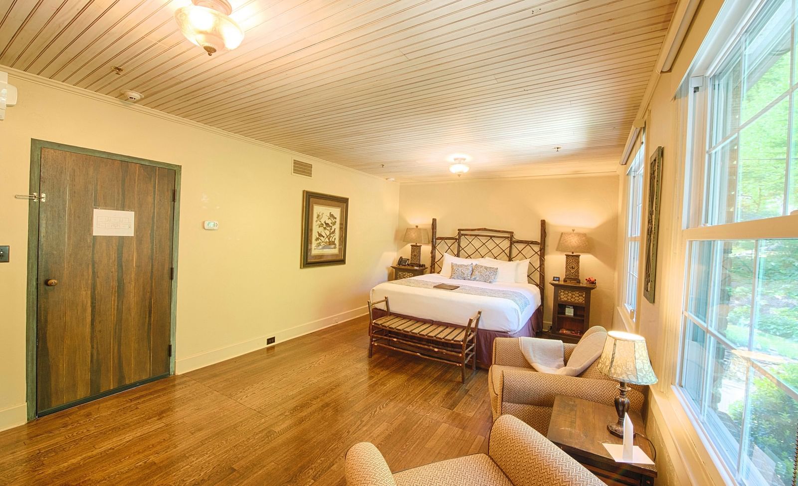 dull view image of a bedroom with a wooden door featuring a plush double bed with two bed side tables on either side of it - Historic Tapoco Lodge
